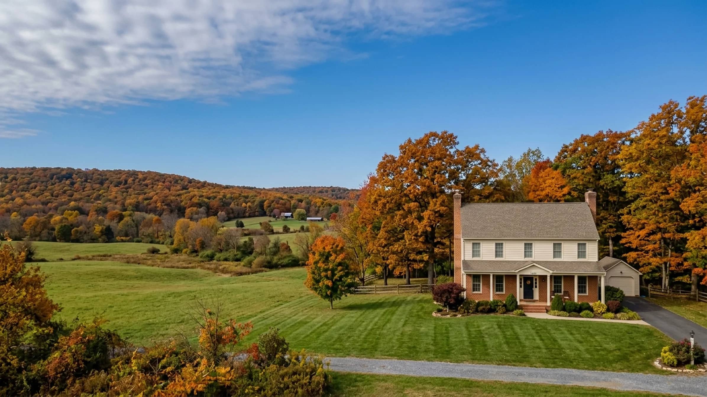 A two-story colonial home on a lawn among autumn trees, with wooded Virginia hills behind it